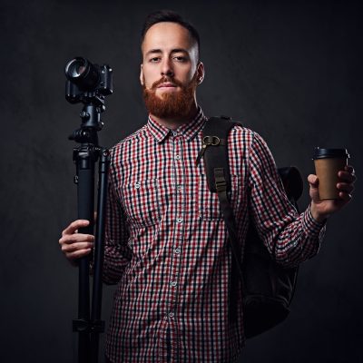 Redhead bearded freelance photographer with tripod and backpack.